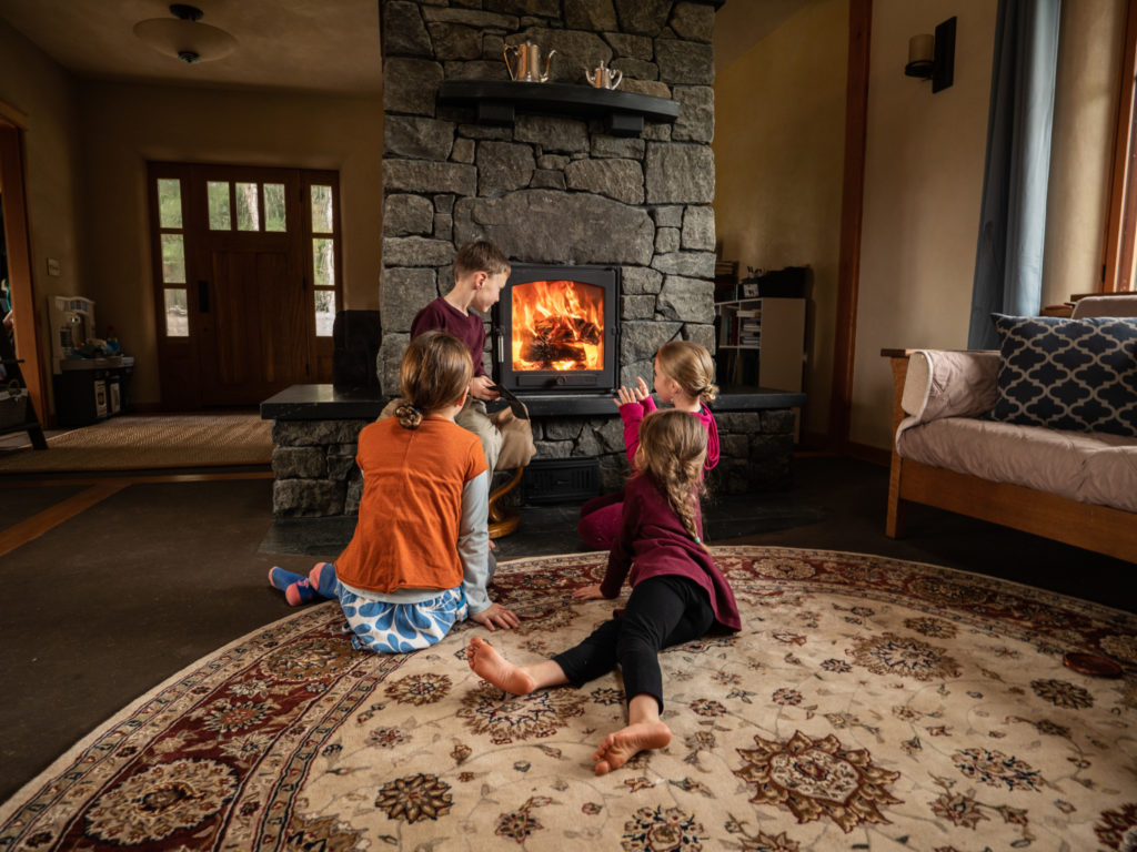 Children sitting next to stone masonry heater in home