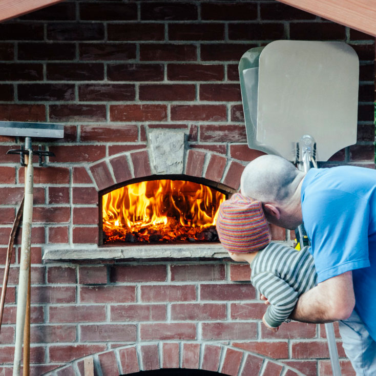 Father and child looking at inside of wood-fired oven